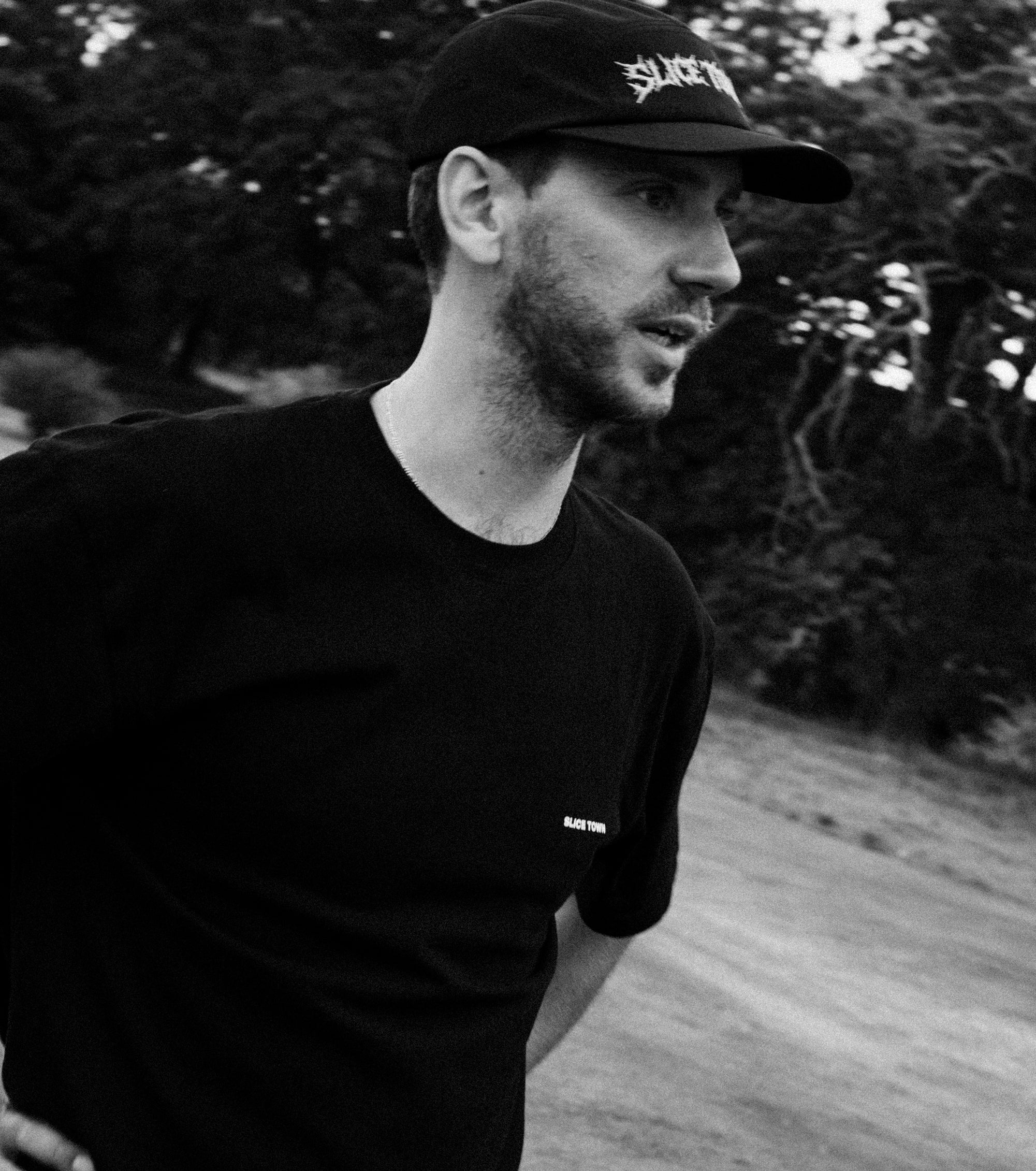 Man wearing a black cap and t-shirt with 'SLICE TOWN' branding outdoors.